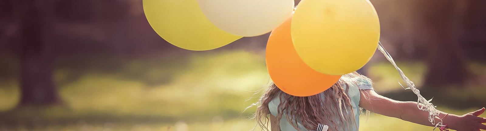 Ung flicka springer med flera gulfärgade ballonger i handen