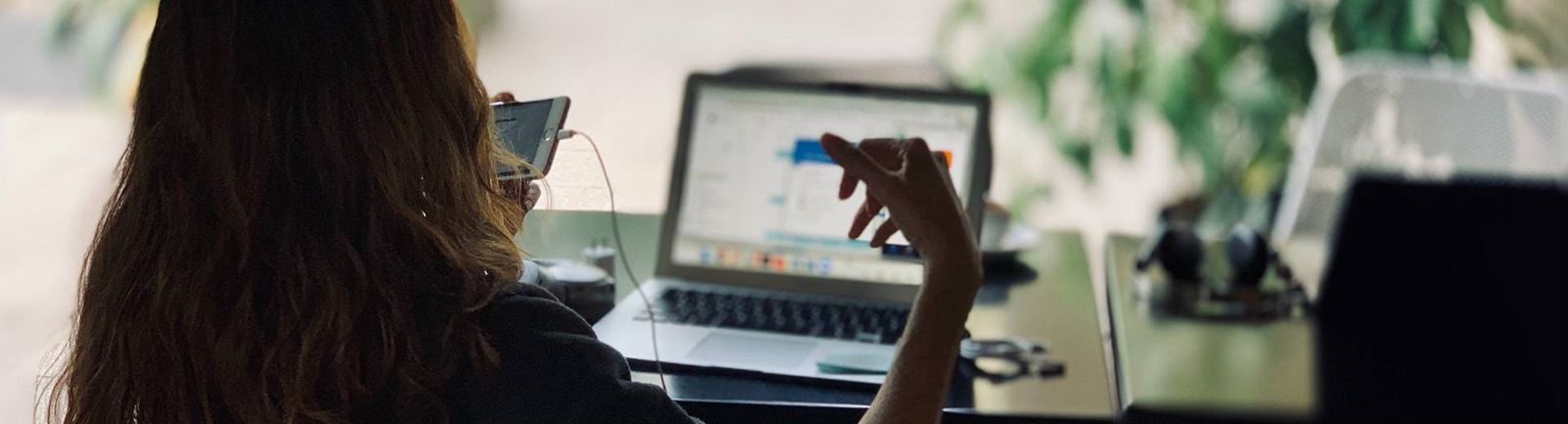 Kvinna sitter framför en dator och pratar i telefon