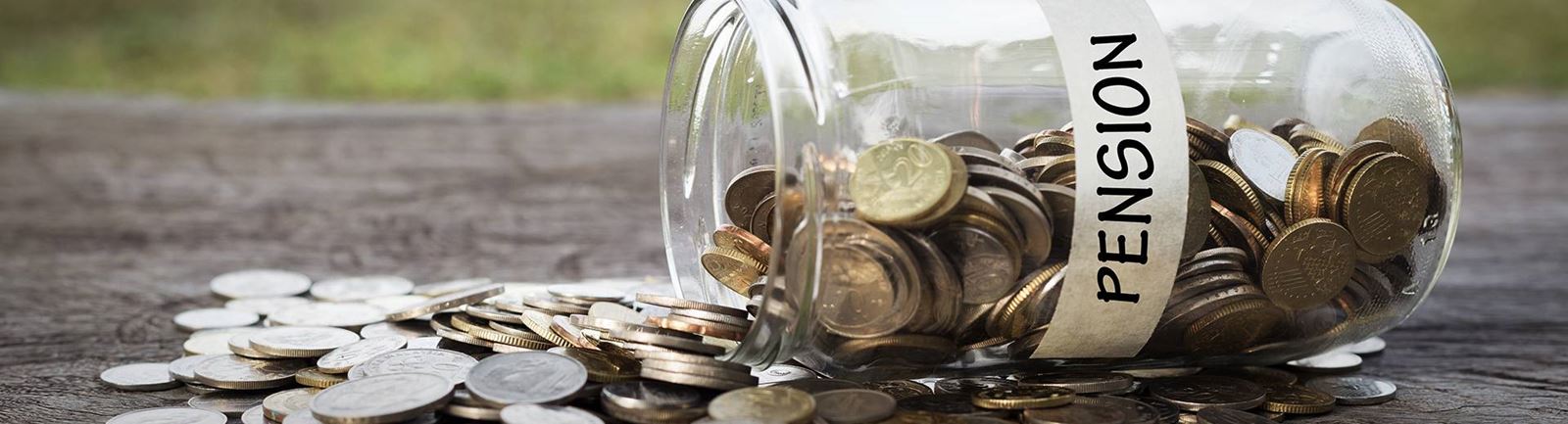 En burk fylld med mynt ligger ner och pengarna har runnit ur burken. Det står Pension på burken.