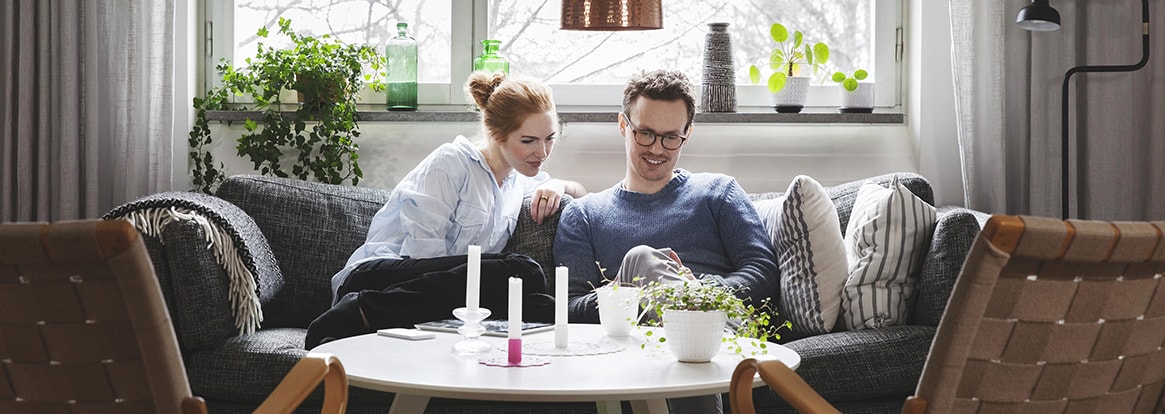 Kvinna och man sitter i en soffa och tittar på mobilen